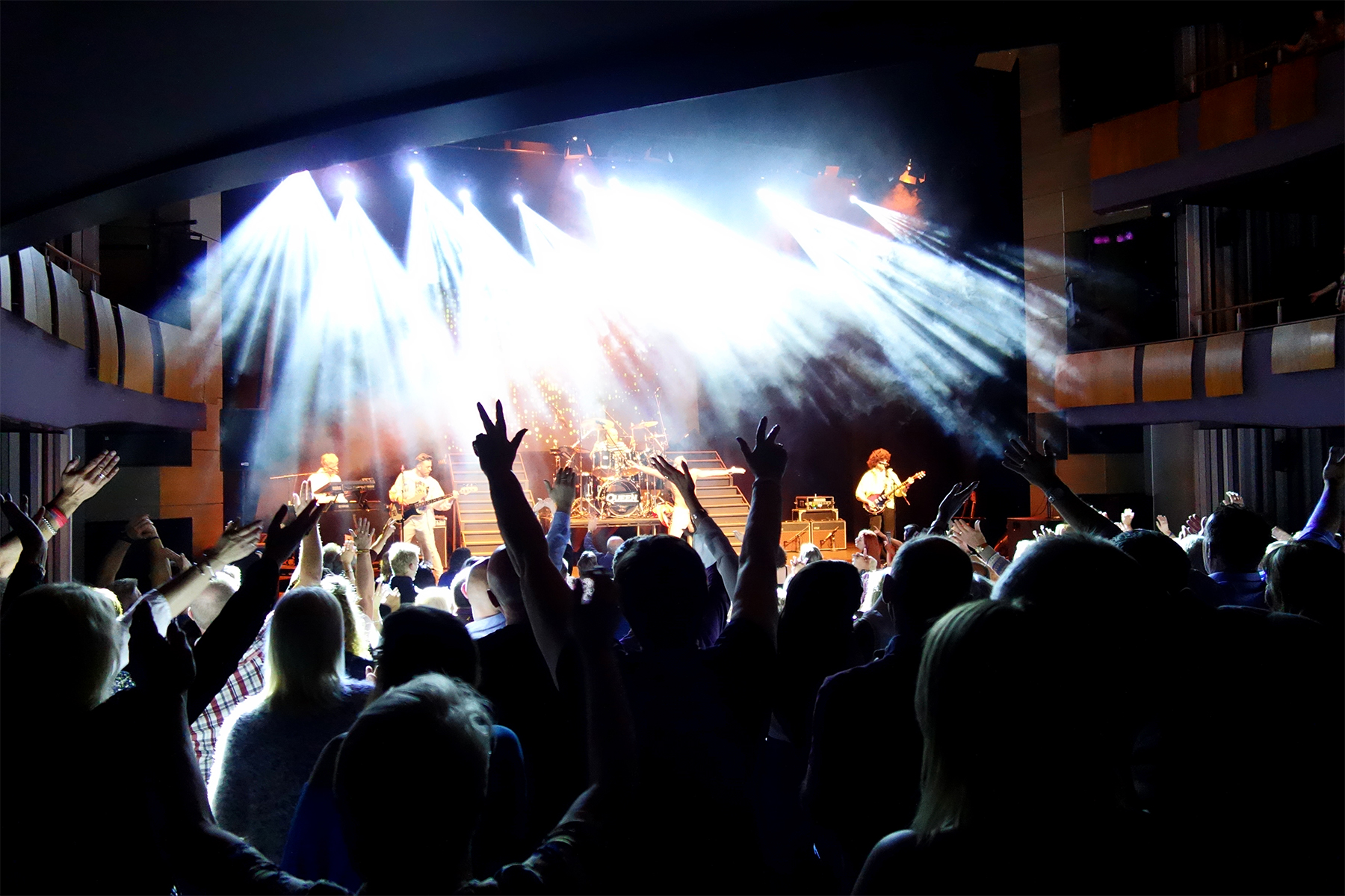 Full band on stage under a burst of white spotlights as fans raise their hands