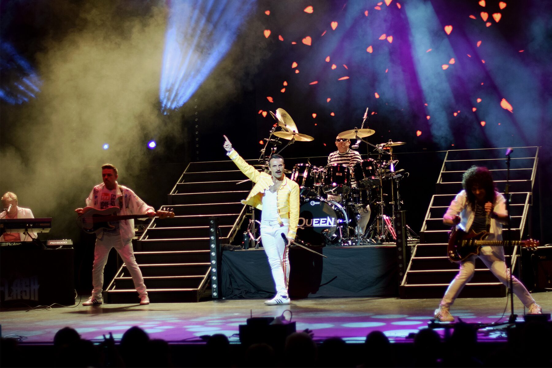 Freddie centre stage in the yellow jacket flanked by the band on the staircase set