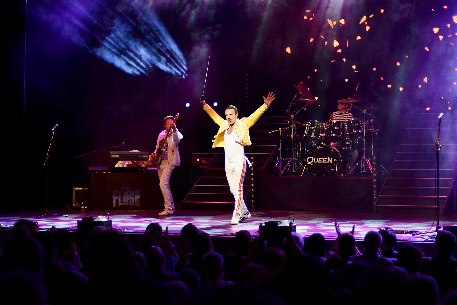 Freddie striding centre stage with sword raised, pyrotechnic sparks falling behind