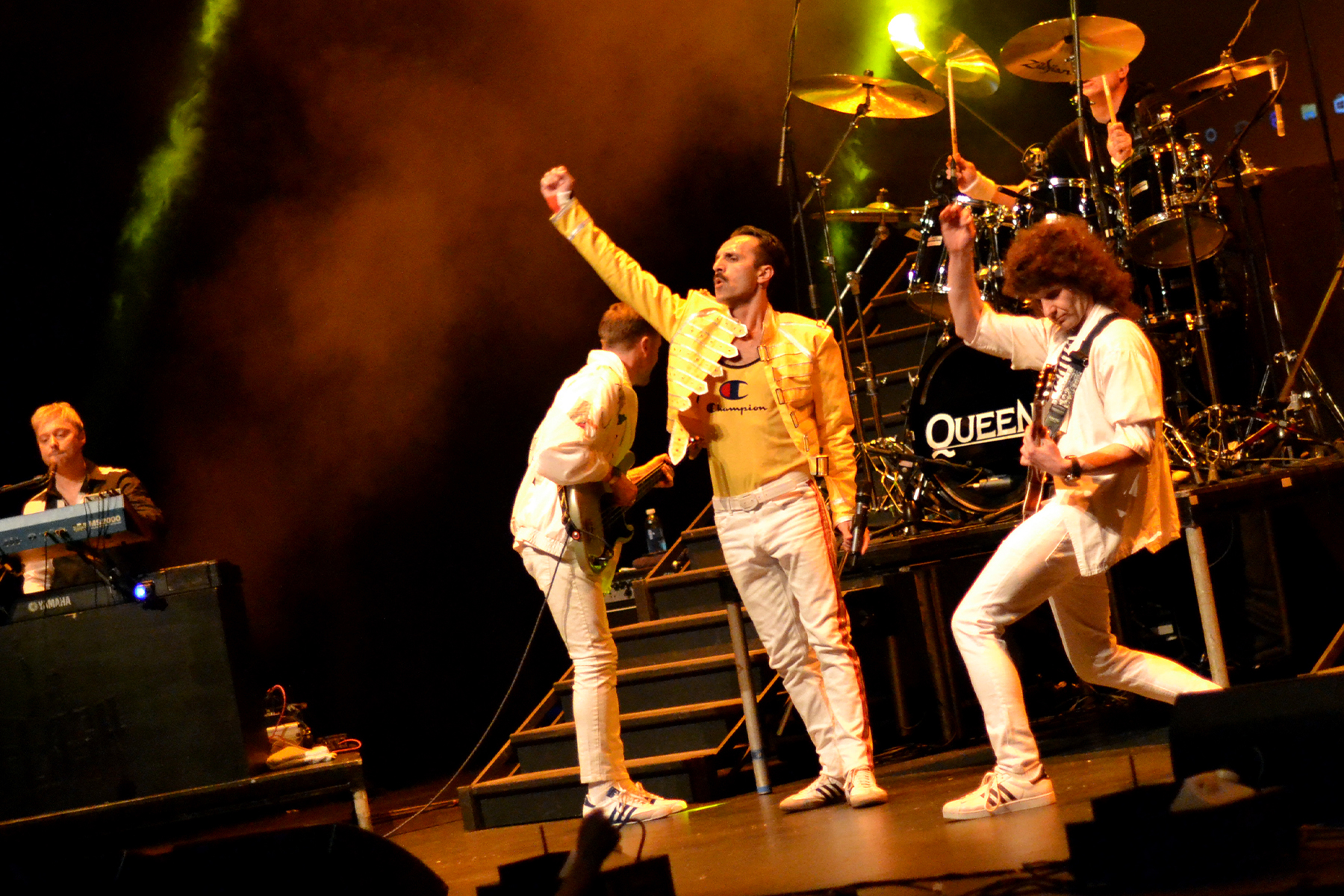 Freddie in the iconic yellow jacket between Brian and the bassist, fist raised