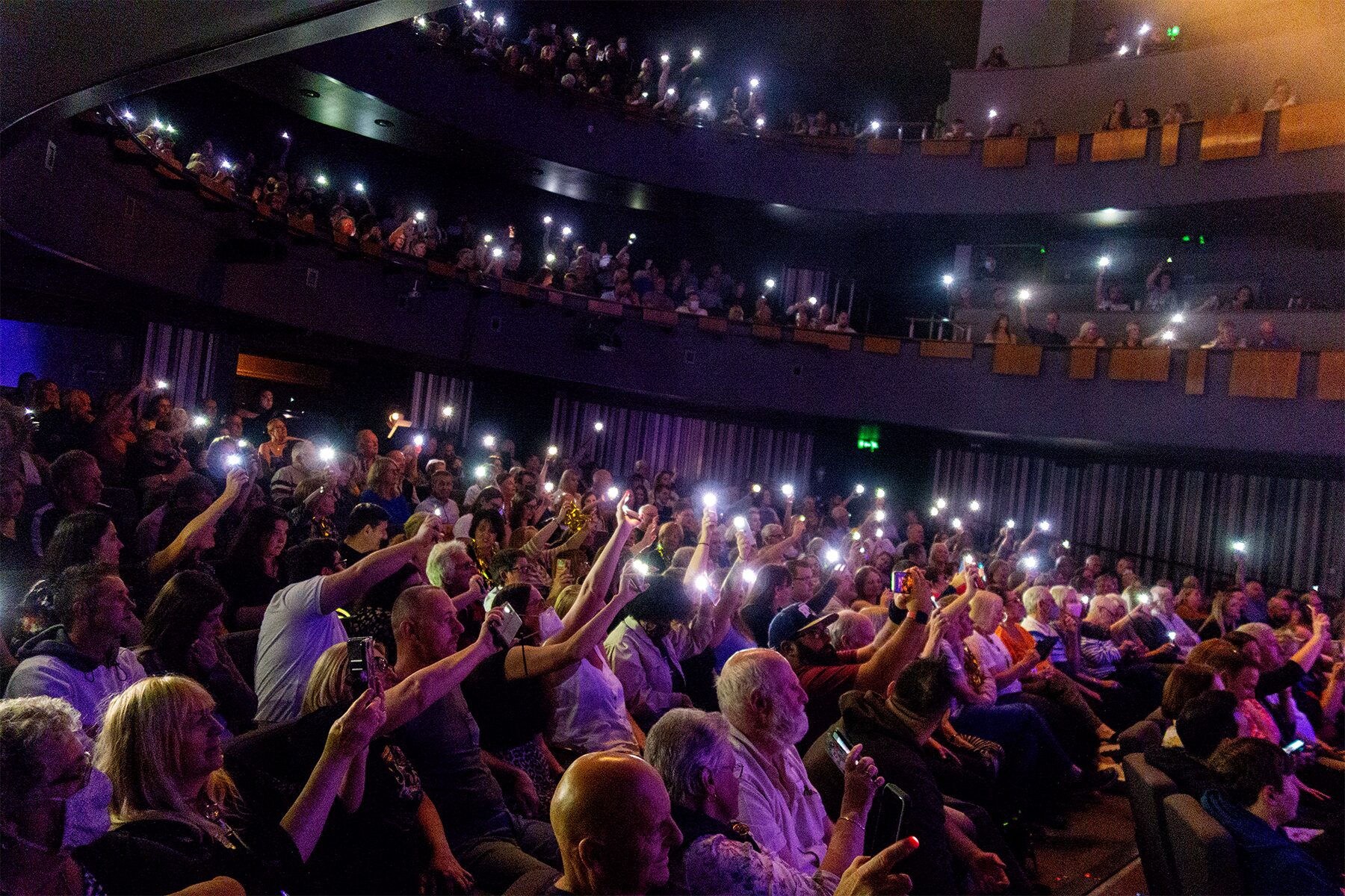 Theatre crowd holding up phone torches across stalls and balconies